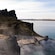 A doorway built into a rocky outcrop, a stone path and stairs descending into a steaming lagoon
